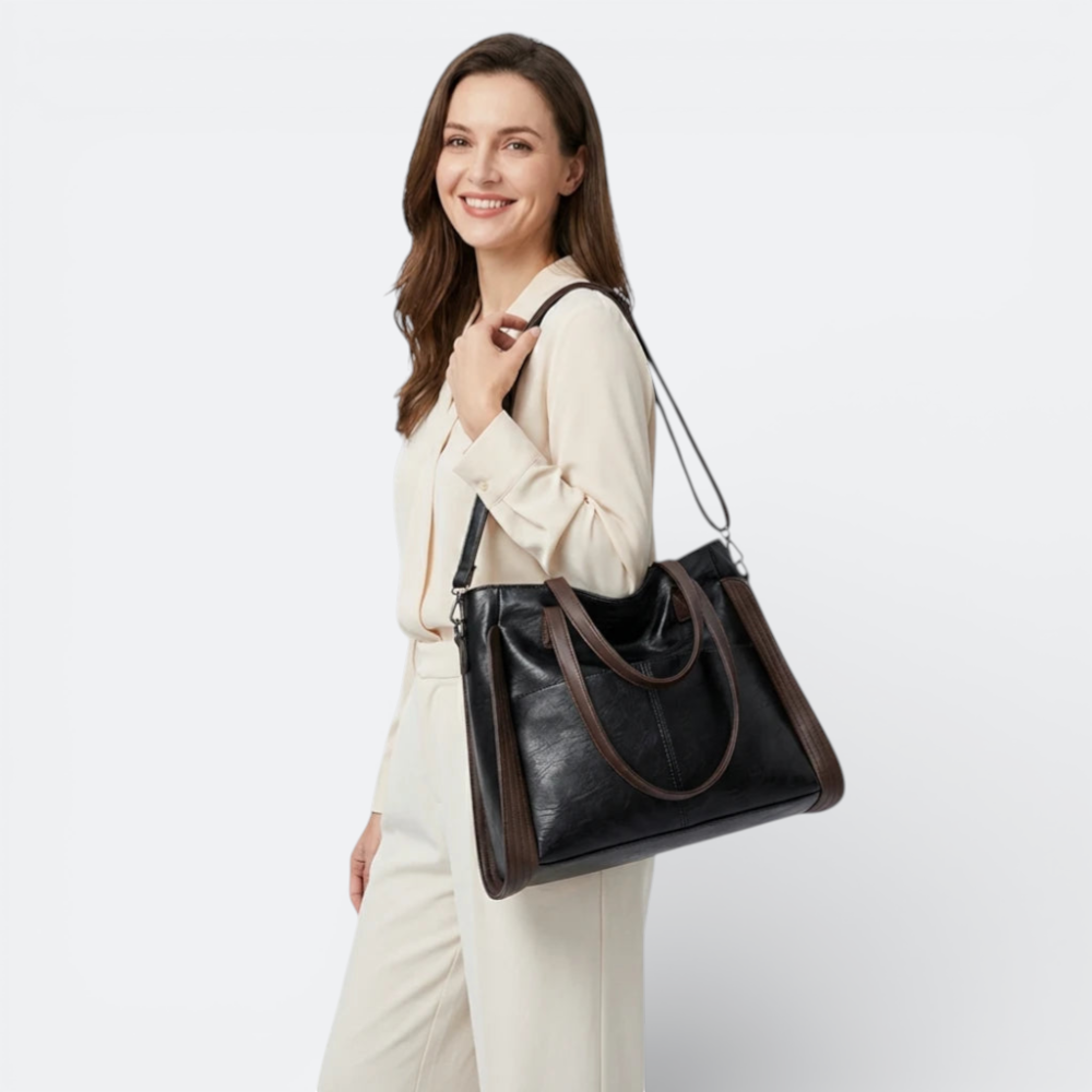 AïtaVia black soft leather tote bag with brown accents and adjustable strap, worn by a woman.