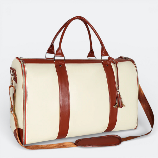 AïtaVia cream duffel bag with brown leather accents, top handles, and adjustable shoulder strap. Features a tassel detail.
