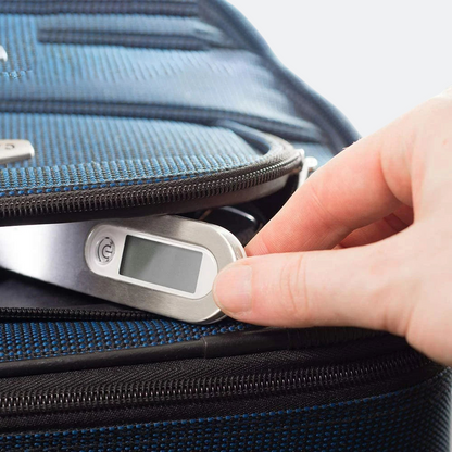 AïtaVia digital luggage scale with a silver finish and LCD screen, being held by a hand near a blue suitcase.