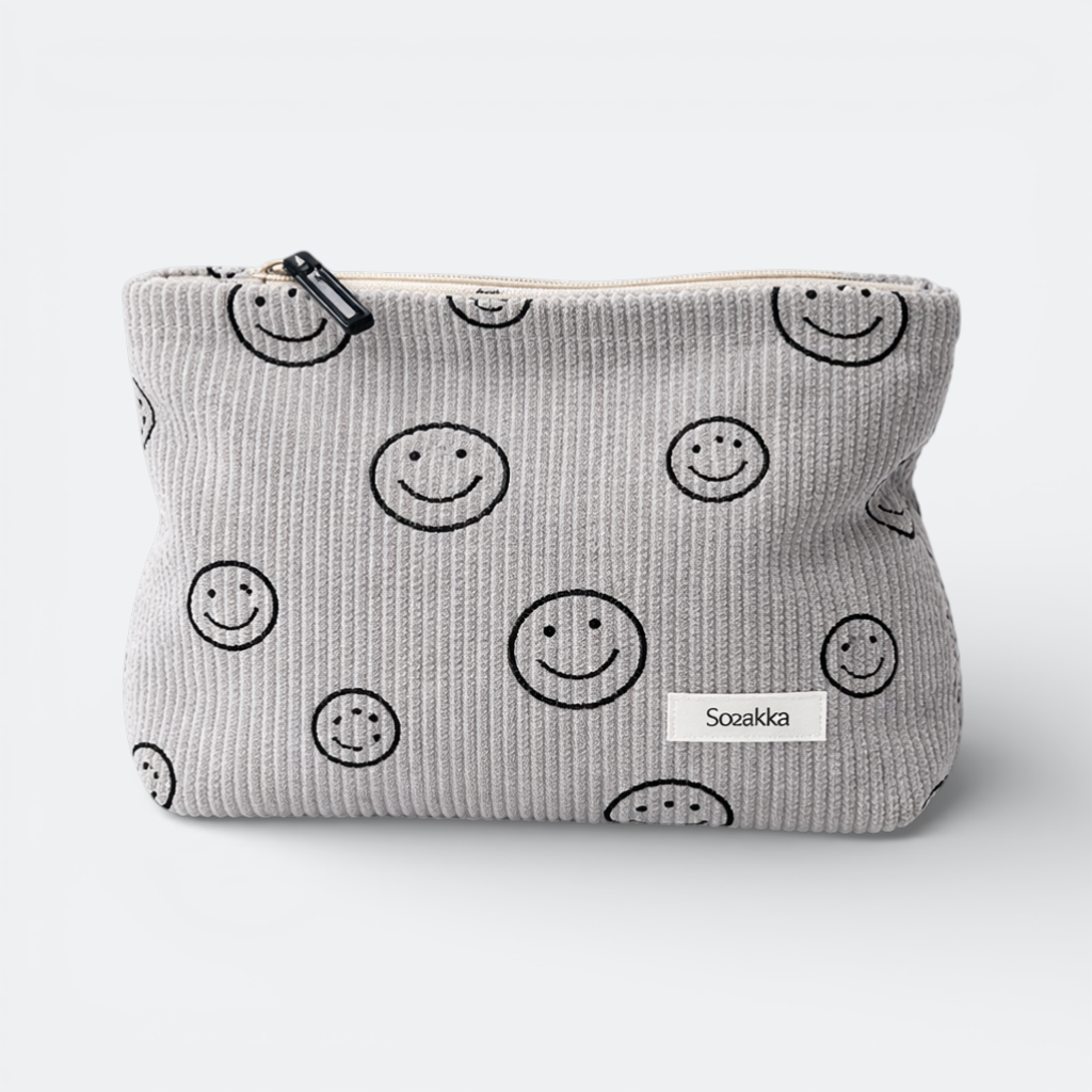 AïtaVia grey corduroy travel toiletry bag with a repeating black smiley face pattern and a white label.