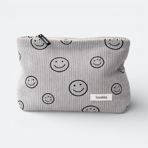 AïtaVia grey corduroy travel toiletry bag with a repeating black smiley face pattern and a white label.