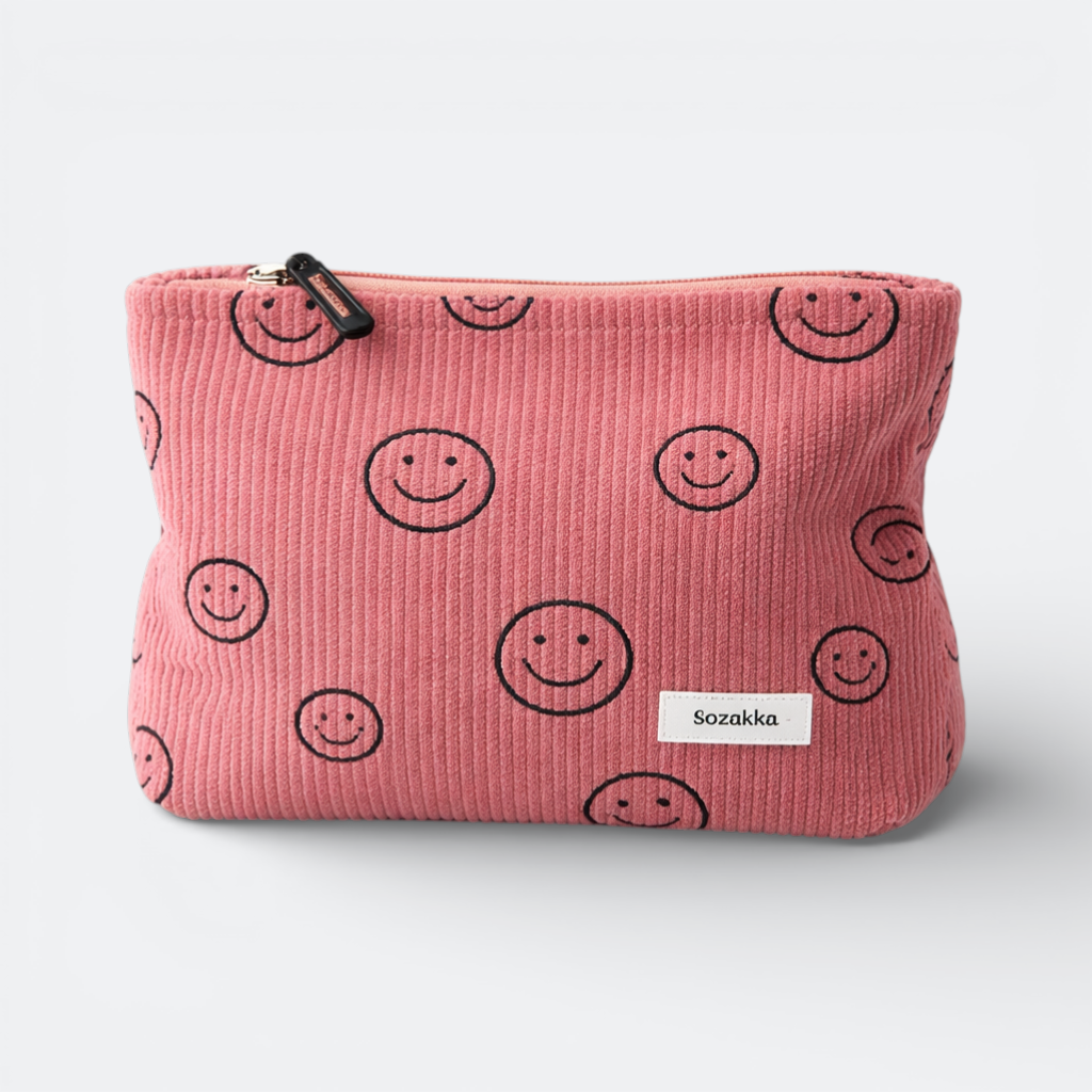 AïtaVia pink corduroy travel toiletry bag with a repeating smiley face pattern and a white label.