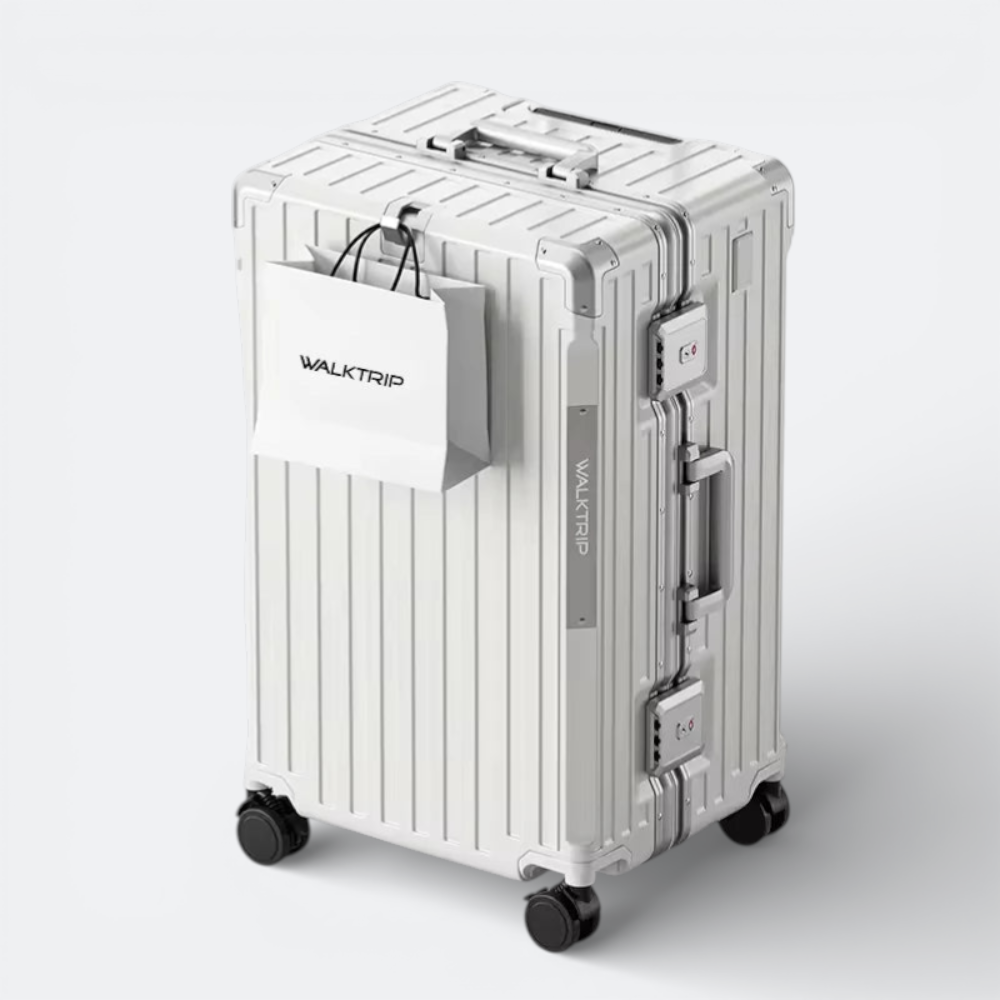 AïtaVia large silver hard-shell suitcase with spinner wheels and TSA lock, featuring a white shopping bag attached.