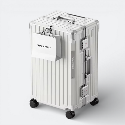 AïtaVia large silver hard-shell suitcase with spinner wheels and TSA lock, featuring a white shopping bag attached.