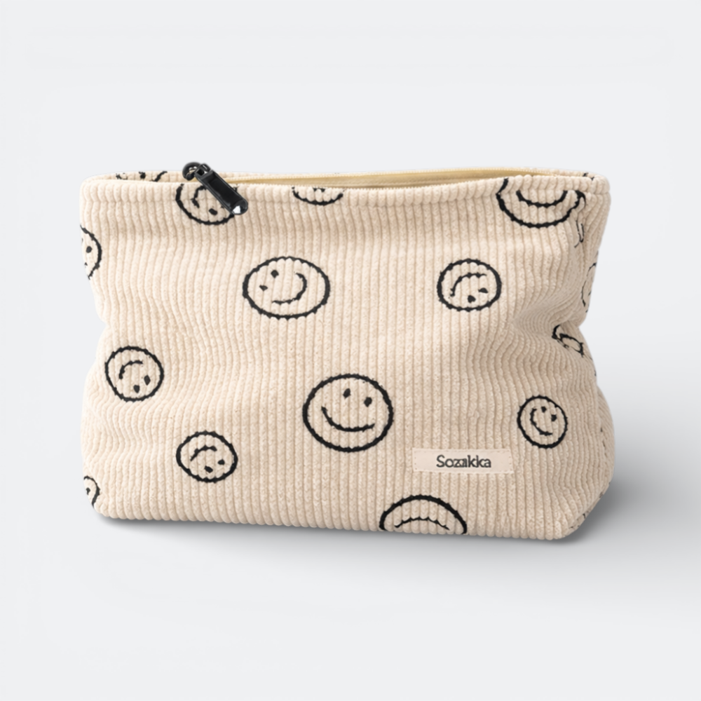 AïtaVia cream corduroy travel toiletry bag with a black smiley face pattern and a zipper closure.