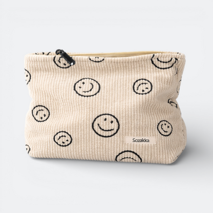 AïtaVia cream corduroy travel toiletry bag with a black smiley face pattern and a zipper closure.