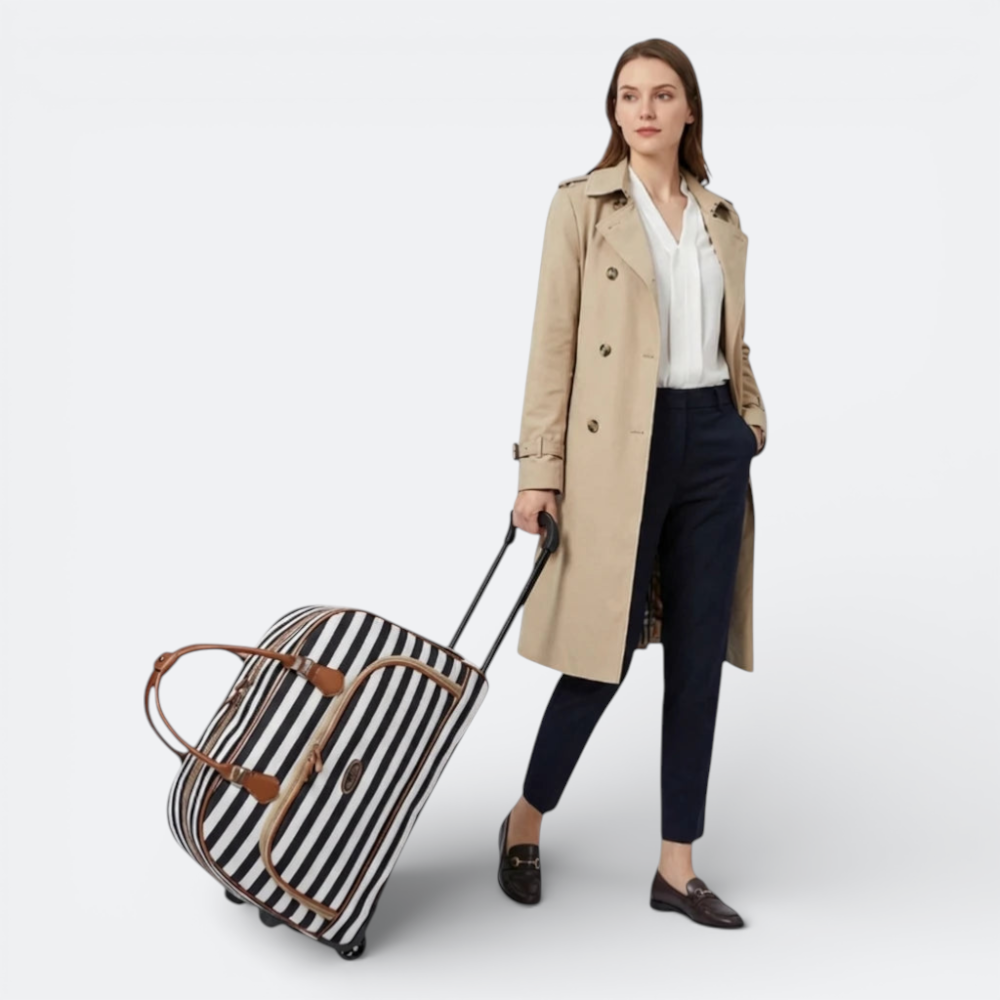 AïtaVia black and white striped soft-sided travel duffel bag with brown leather accents, pulled by a woman in a trench coat.