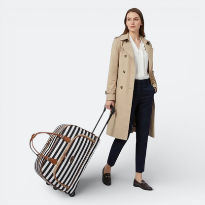 AïtaVia black and white striped soft-sided travel duffel bag with brown leather accents, pulled by a woman in a trench coat.