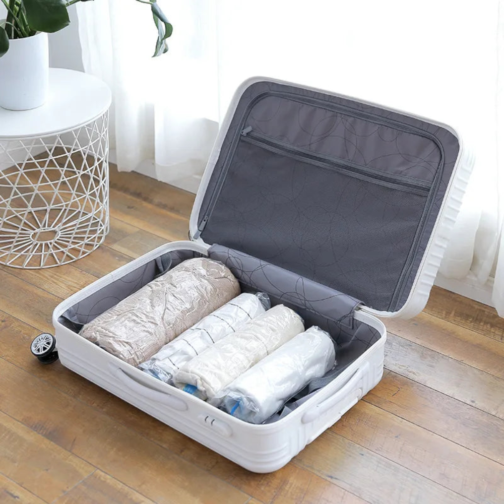 AïtaVia vacuum-seal compression bags in beige and white, neatly rolled inside an open white suitcase.