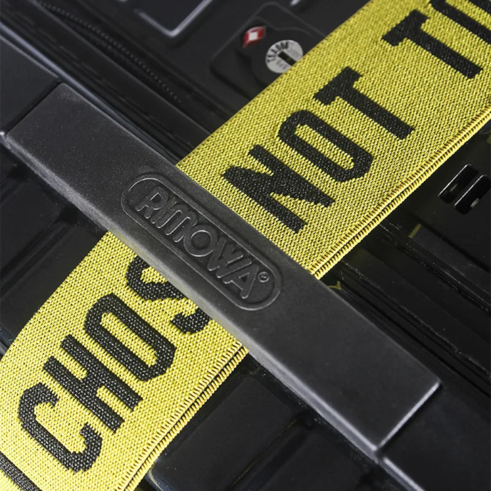 AïtaVia yellow luggage strap with black text "CHOS NOT TO" and a black buckle with embossed logo.